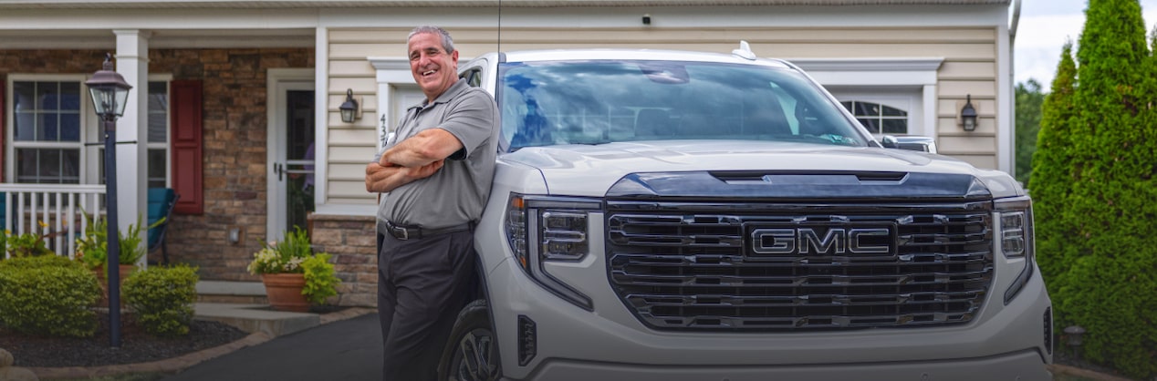 Marco C. leaning on his GMC Sierra truck that is parked in his driveway