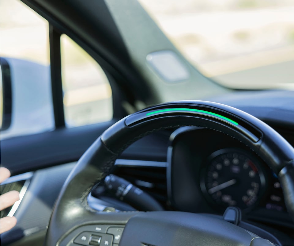 A close-up view of the Cadillac XT6 steering wheel shows a green light bar, indicating Super Cruise is active.
