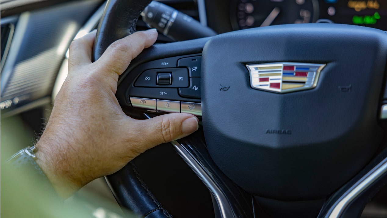A close-up shows a hand lightly resting on the Cadillac XT6 steering wheel with the Cadillac emblem visible.