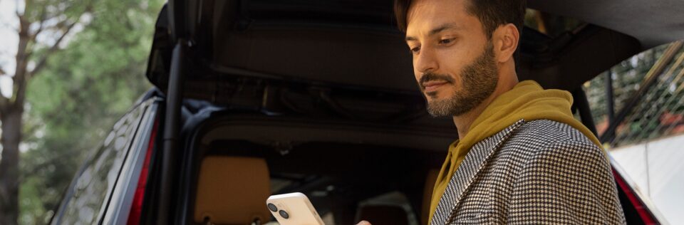 Man Standing Next to Opened Vehicle Tailgate Using Smartphone