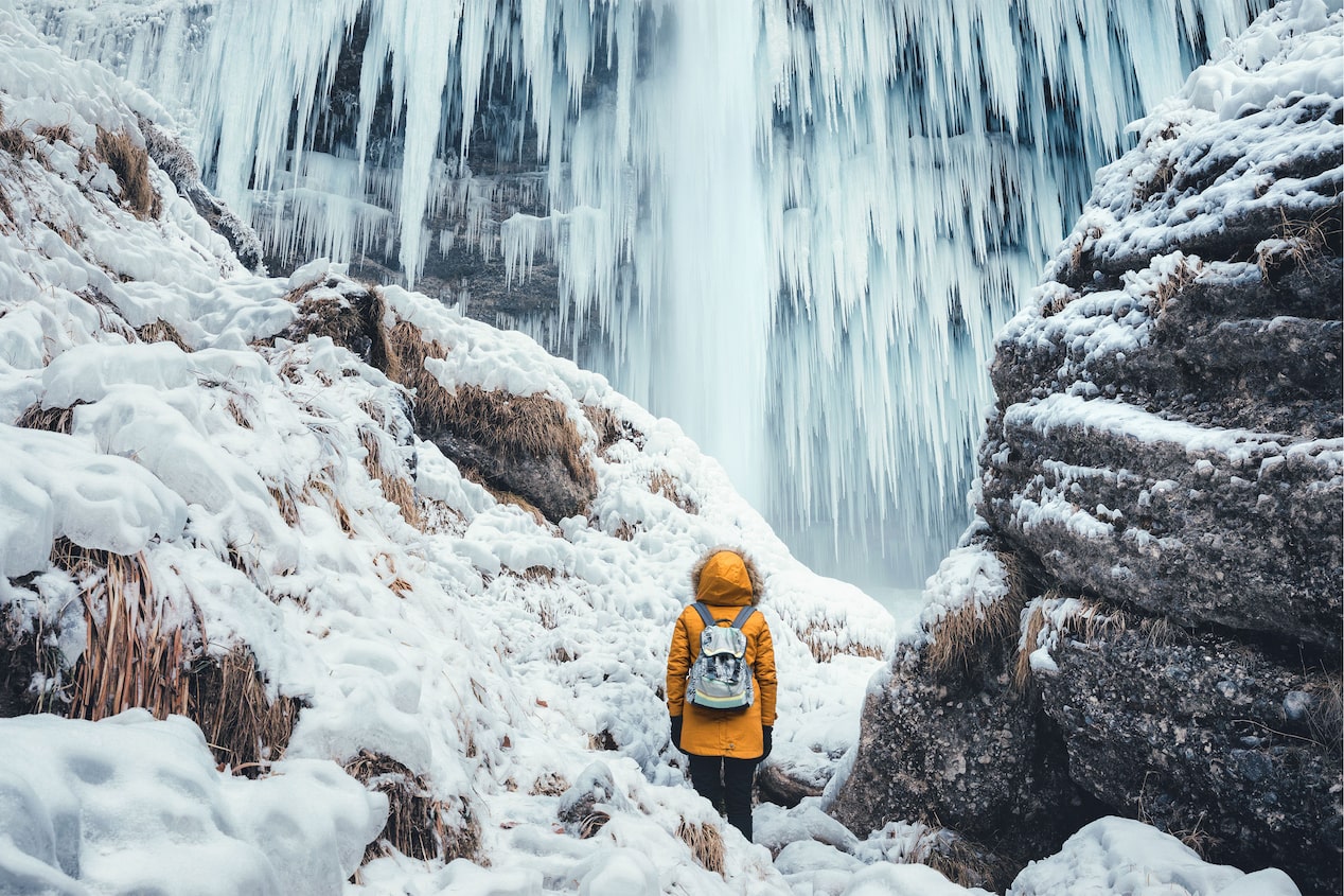 Hiker Sitting Next to the Base of an Ice Cave