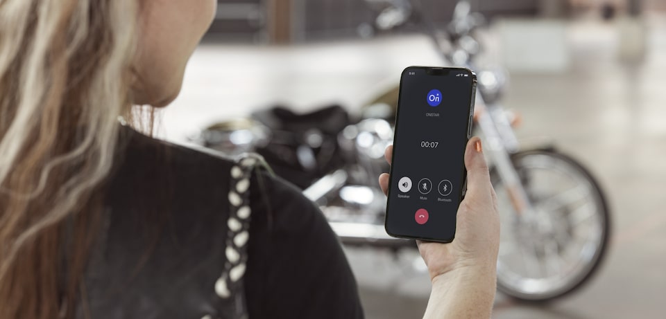 Female Motorcycle Driver Checking the OnStar Guardian App Next to her Bike