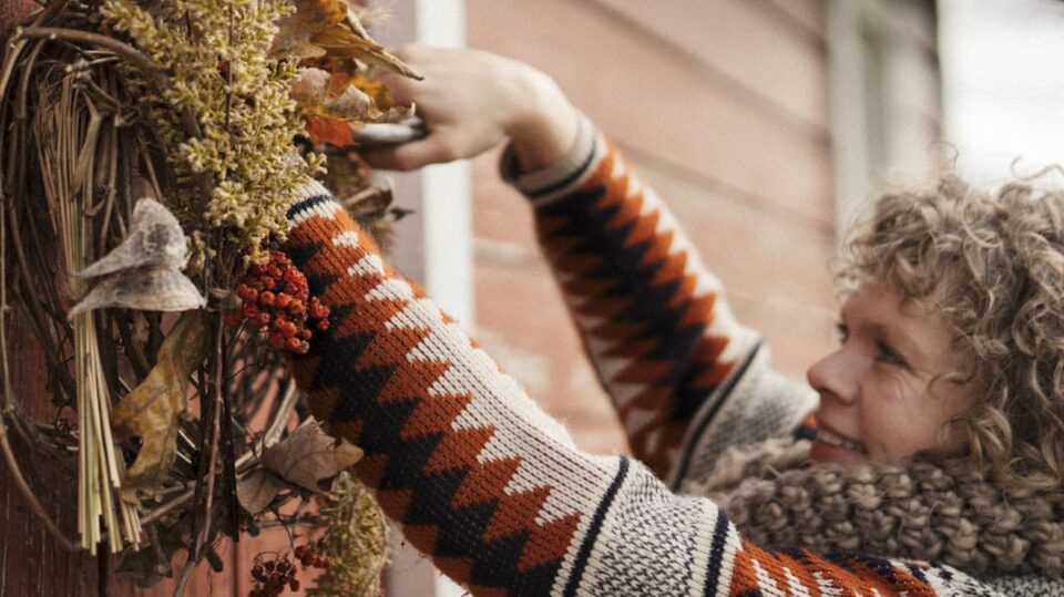 Woman Hanging a Fall Wreath on Her Home Exterior