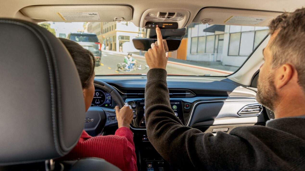 Back Seat View of a Male Passenger Pushing The OnStar Button on a Rear View Mirror