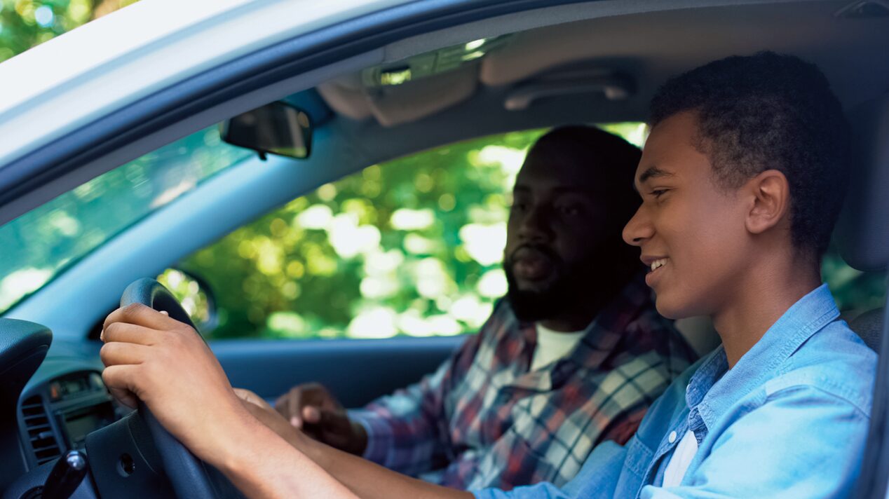 Teenager Sits in Driver’s Seat with Both Hands on the Steering Wheel & Stares Straight Ahead