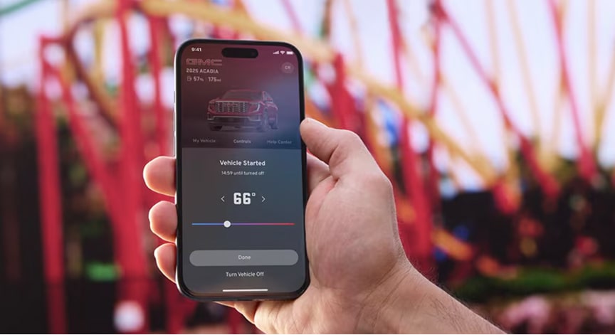 A hand holds a smartphone displaying the myGMC app showing a remotely started GMC vehicle at 66 degrees.