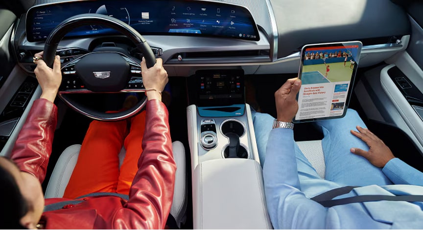 An overhead view inside a Cadillac vehicle with one person driving and another using a tablet.