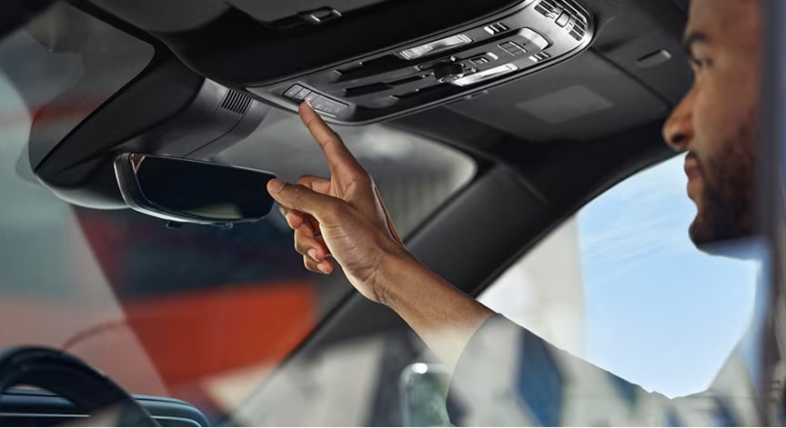 A person's hand reaches up to press a button on the car's overhead console for assistance.