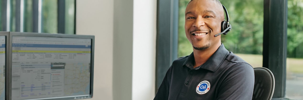 A male OnStar service advisor sitting at his desk smiling and wearing his headset