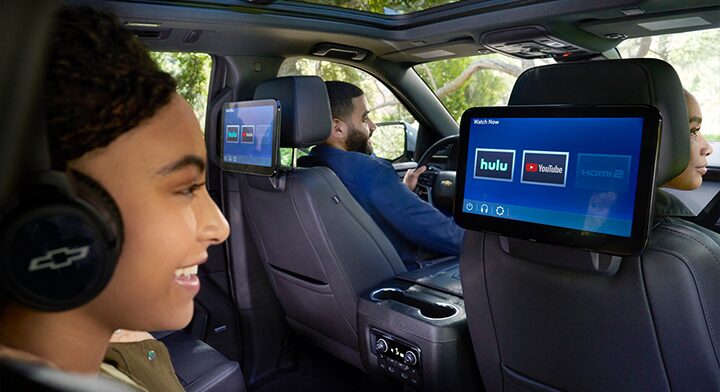 A girl sitting in the passenger seat looking at a tablet device attached to the seat in front of her.