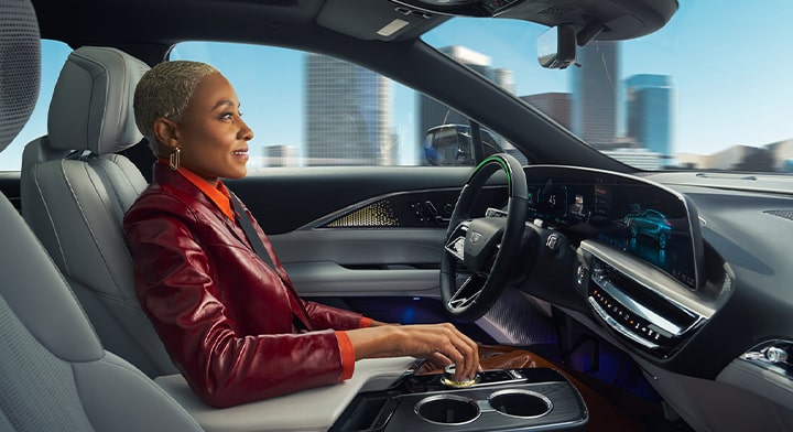 A woman sitting in the driver's seat of a vehicle with her right arm resting on the center console.